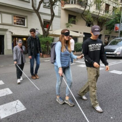 Fotografia de 4 persones creuant un pas de vianants. Les persones van en parelles, un integrant de la parella té discapacitat visual i és usuària de bastó.