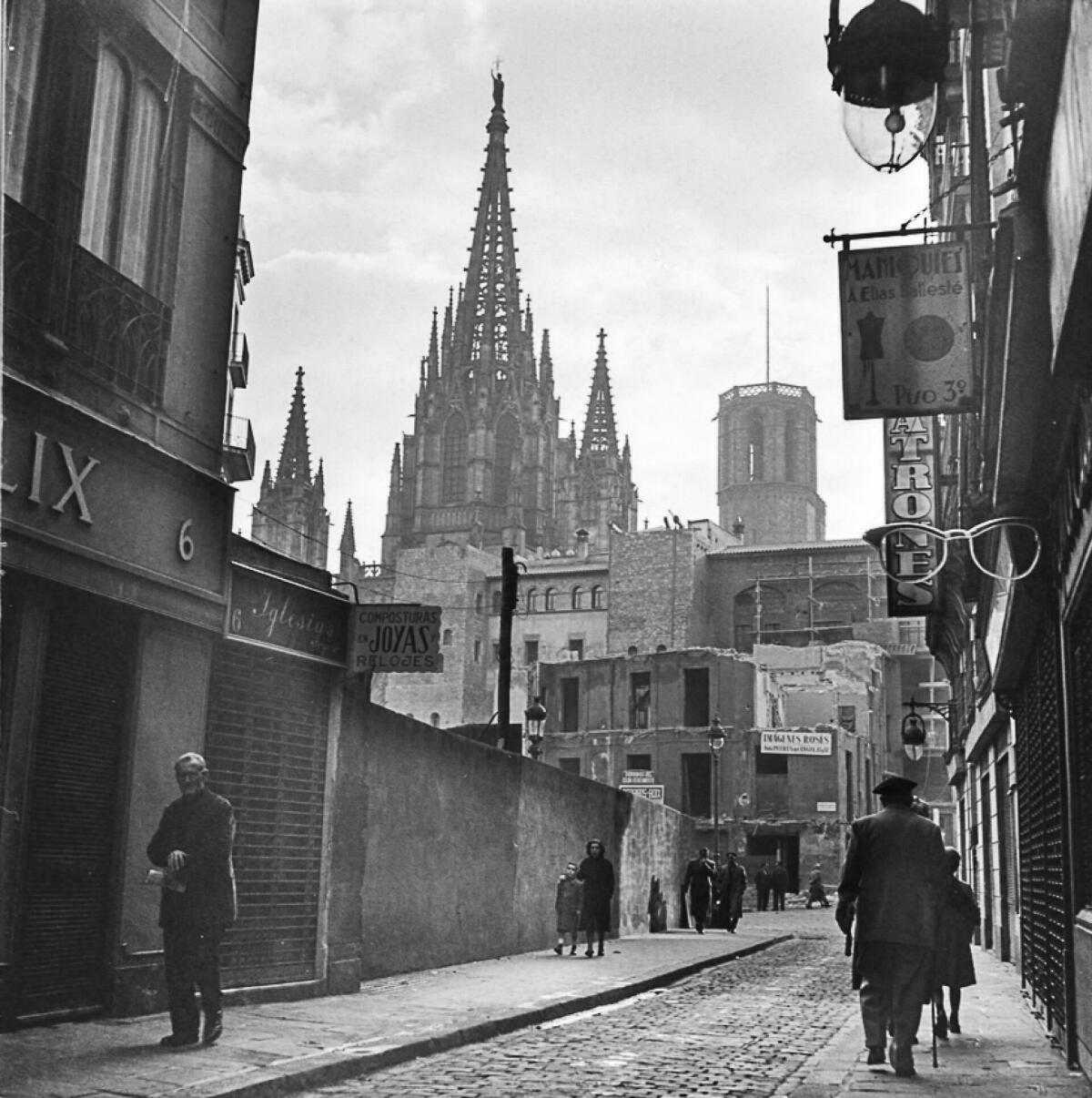 Foto en blanc i negre. Es veu el carrer dels Arcs amb la Catedral al fons i gent caminant