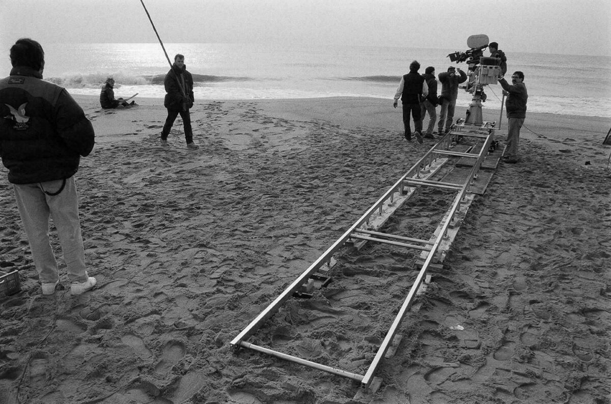 Foto en blanc i negre. Es veu el director de cine rodant una escena a la platja