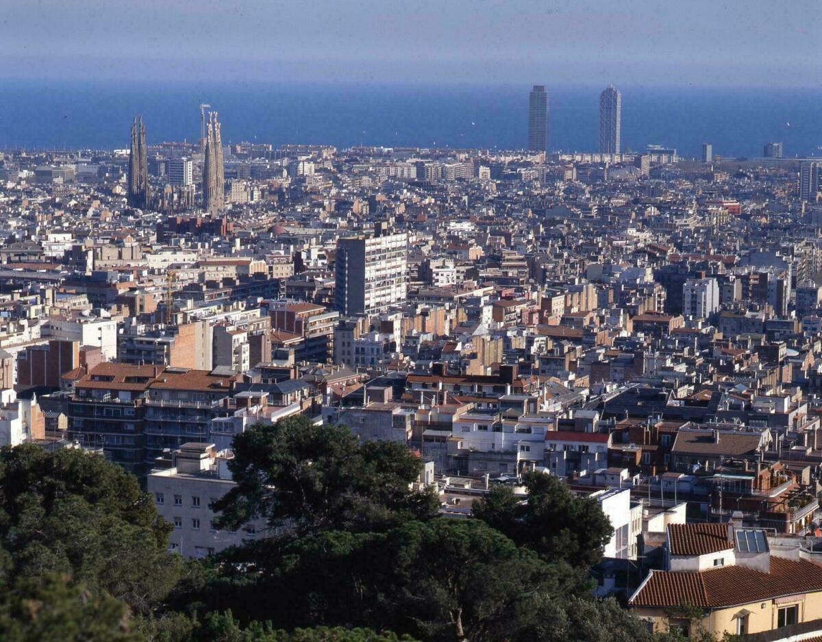 Foto en color. Vista de Barcelona des del Parc Güell, Destaquen l´edifici de la Sagrada Família, les torres de la Vila Olímpica i el mar al fons.