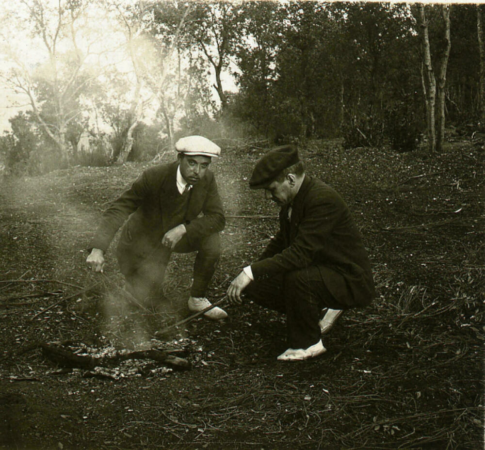 Foto en blanc i negre. Es veuen 2 senyors fent una foguera al bosc