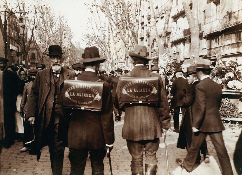Venedors ambulants de 'la Sombrereria La Alianza ' caminant per la Rambla amb carteres a l'esquena, 1907-1908. AFB. Frederic Ballel