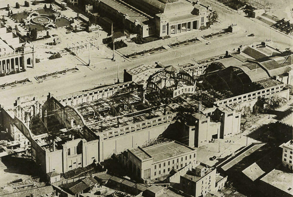 Foto en blanc i negre. Vista aèria de les obres del Palau de la Metal·lúrgia de Montjuïc. Es veu el Palau en obres, sense  la coberta