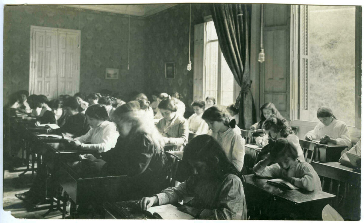 Foto en blanc i negre. Es veu una aula de l'Institut de Cultura per a la Dona amb dones i nenes assegudes davant de pupitres