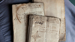 Tres libros antiguos superpuestos entre sí con las cubiertas manuscritas. En la cubierta del libro de primer plano se observa el dibujo del señal heráldico de la ciudad de Barcelona.