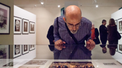 A man carefully observing an exhibition photograph, leaning gently against a glass case