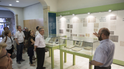 A group of people listening to explanations given by another person in a room with information panels and glass cases with documents