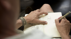 A man’s hand holding a sketchpad while the other hand draws
