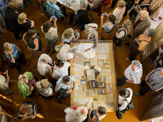 Vista zenital d’un grup de persones col·locades al voltant d’una taula que exposa tota una sèrie de documents