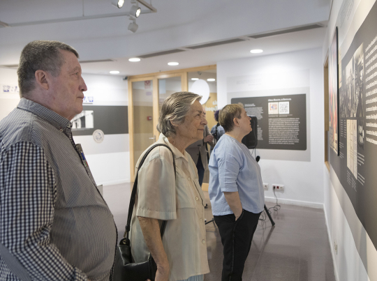 Diverses persones dretes observen uns plafons amb información a la sala d’exposicions de l’edifici Jaume Fuster, lloc on es troba l’AMDG