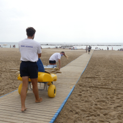 Personal técnico desplazando a una persona hasta la playa con una silla amfibia. 