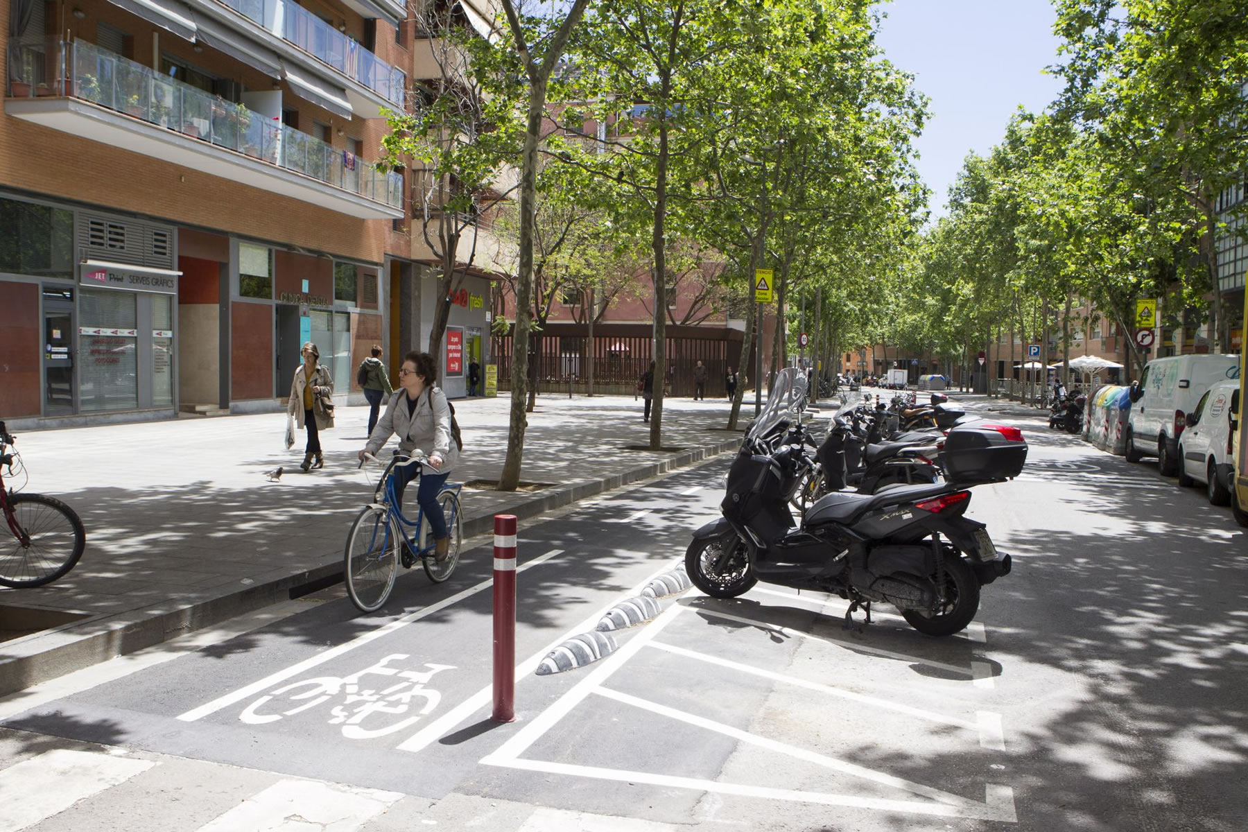 A woman on bicycle in a bicycle lane parallel to a motorcycle parking zone off the pavement