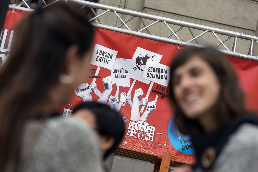 Dues dones davant del cartell de la campanya Som comerç just i banca ètica. 