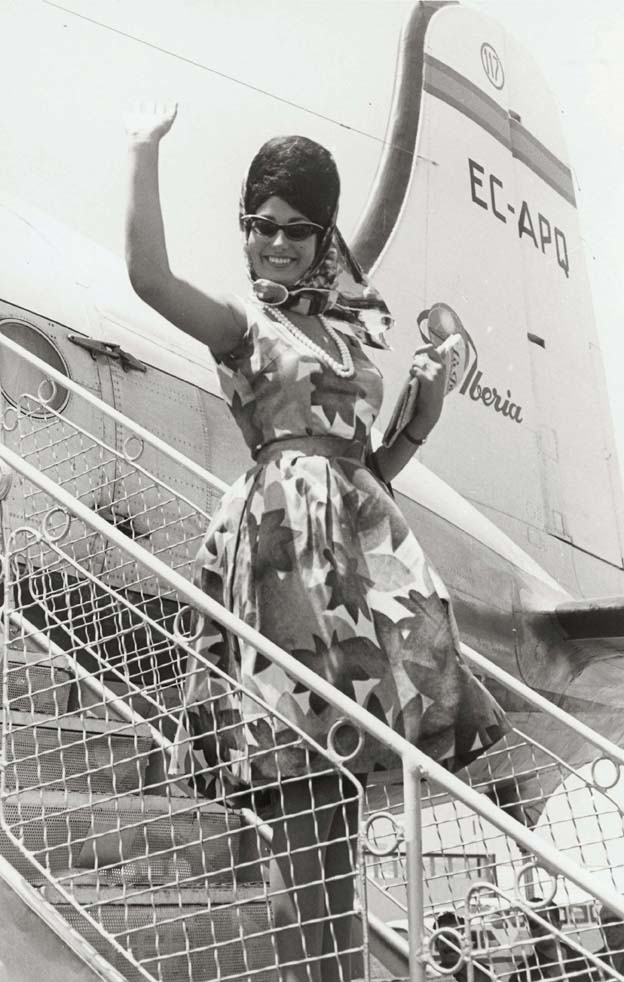 Foto en blanc i negre de Miss Europa saludant, somrient i baixant les escales de l'avió a la seva arribada a l'aeroport de Prat
