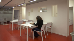 A person sitting at a table consulting documents in a white room with another table