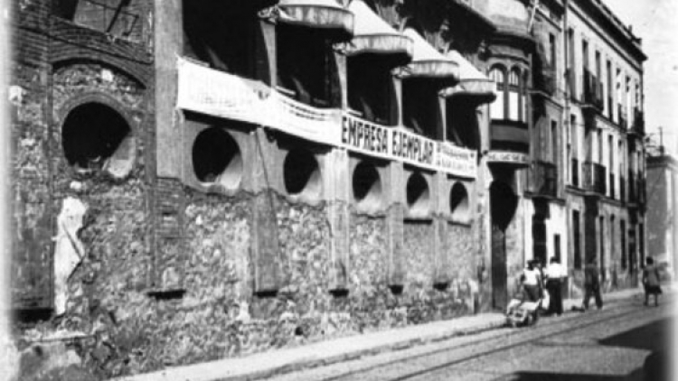 Fotografia on s'observa la façana de l'empresa "Cristalleries Planell" a base d'un primer pis adornat mitjançant òculs i, en el pis de sobre, s'obren cinc balcons amb els seus respectius tendals.   