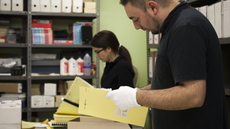 Dos personas con guantes revisan expedientes en una sala de trabajo de un archivo