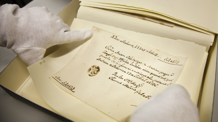 Unas manos con guantes blancos sujetan un documento manuscrito