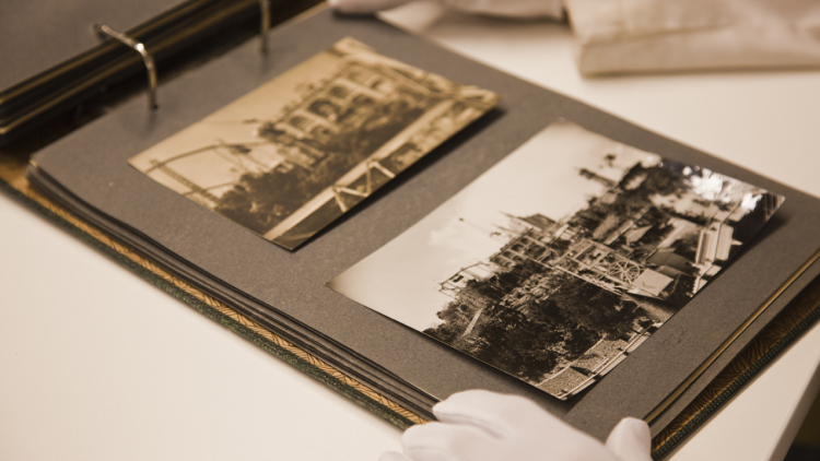 Unas manos con guantes blancos están colocadas sobre un álbum de fotografías abierto que muestra dos imágenes en blanco y negro