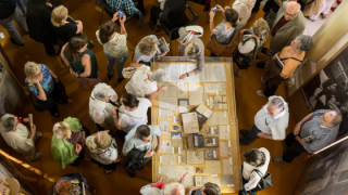 Vista zenital d’un grup de persones col·locades al voltant d’una taula que exposa tota una sèrie de documents
