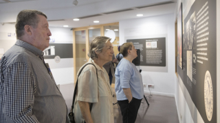 Varias personas de pie observan unos paneles con información en la sala de exposiciones del edificio Jaume Fuster, lugar donde se encuentra el AMDG