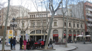 Un grupo de alumnos de Primaria se encuentran rodeando un educador mientras escuchan sus explicaciones. Todo el grupo se encuentra en medio de la plaza frente al Casino de la Alianza del Poblenou.