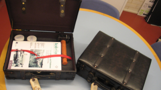 Two briefcases on a table, one of them is open and contains teaching materials for the activity about the Macosa Factory.