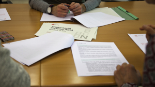 Se ve una mesa durante una reunión, con varios documentos abiertos encima la mesa