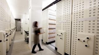 Sala d’armaris compactes d’un arxiu amb una persona caminant amb una caixa a les mans