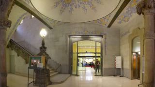 Un vestíbul decorat amb pintures florals, amb una escala a mà esquerra i dues portes, la frontal dóna accés a una sala de recepció