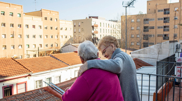 dues dones grans s'abracen i es donen suport en una terrassa amb vistes a la ciutat