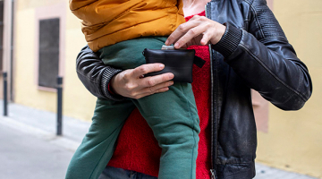 una mujer con un niño en brazos sostiene su cartera con las manos y extrae un billete del interior