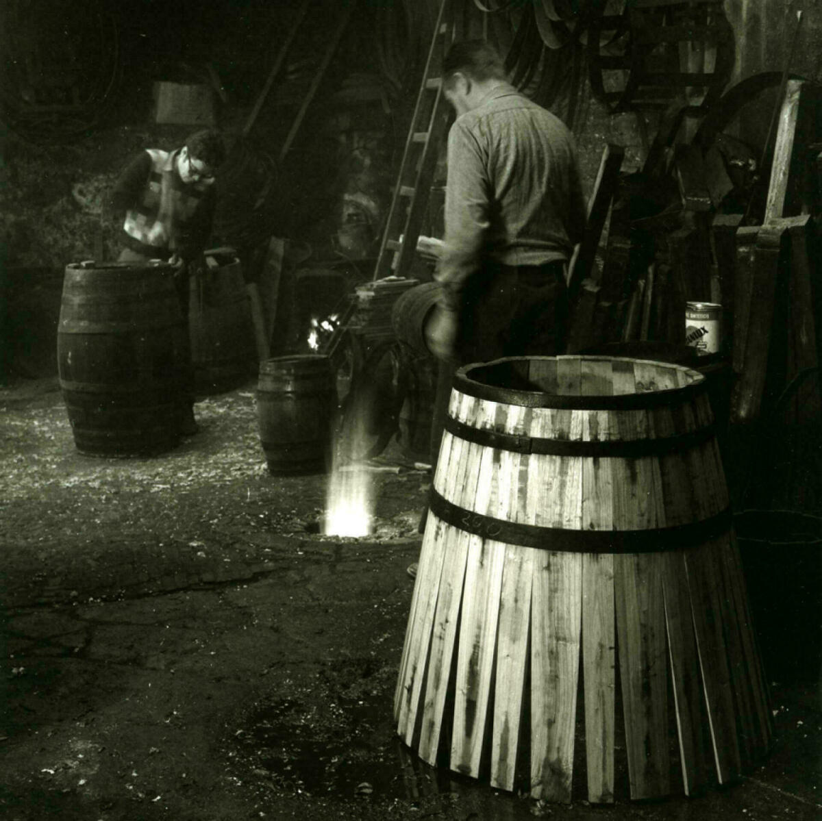 Foto en blanc i negre. Es veuen 2 artesans fent botes de vi en el seu taller